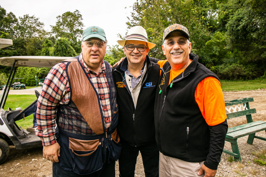 Three men smiling outdoors near golf cart