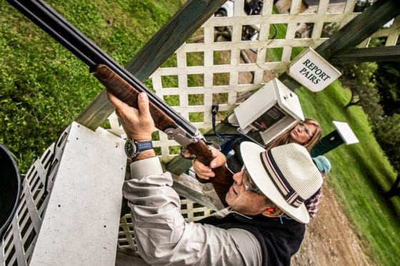 Man in hat aiming shotgun at clay target