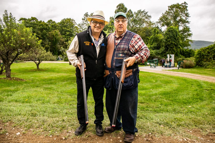 Two men posing with shotguns on grassy field