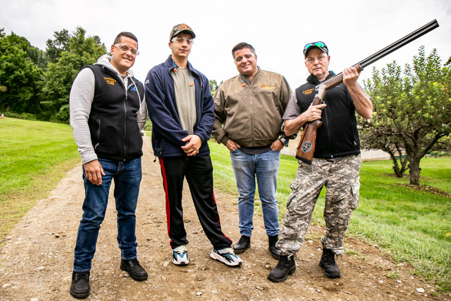Four men outdoors, one holding a shotgun