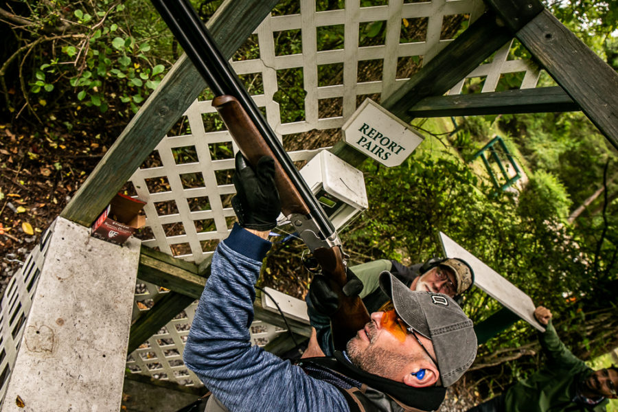 Shooter aiming shotgun at outdoor clay target station