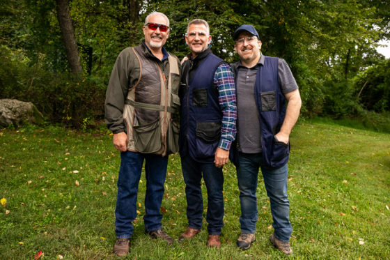 Three men smiling outdoors in vests