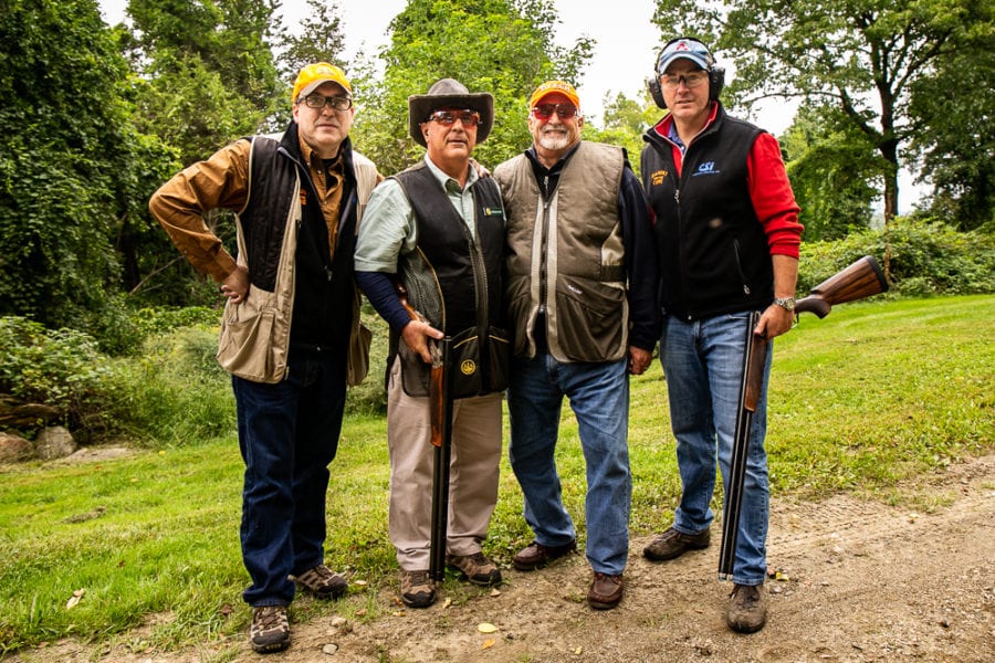 Four men posing with shotguns outdoors