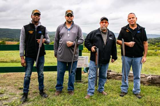 Four men standing outdoors holding shotguns