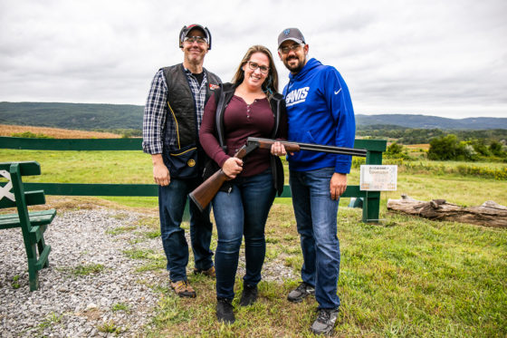 Three people at outdoor shooting range with shotgun