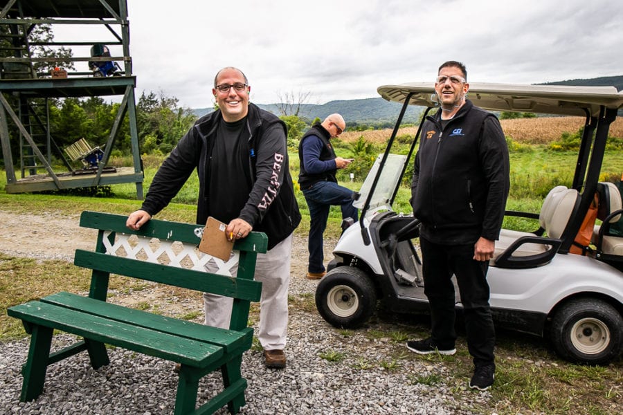 Three men standing by golf cart and bench