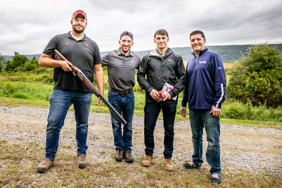 Four men outdoors, one holding a shotgun