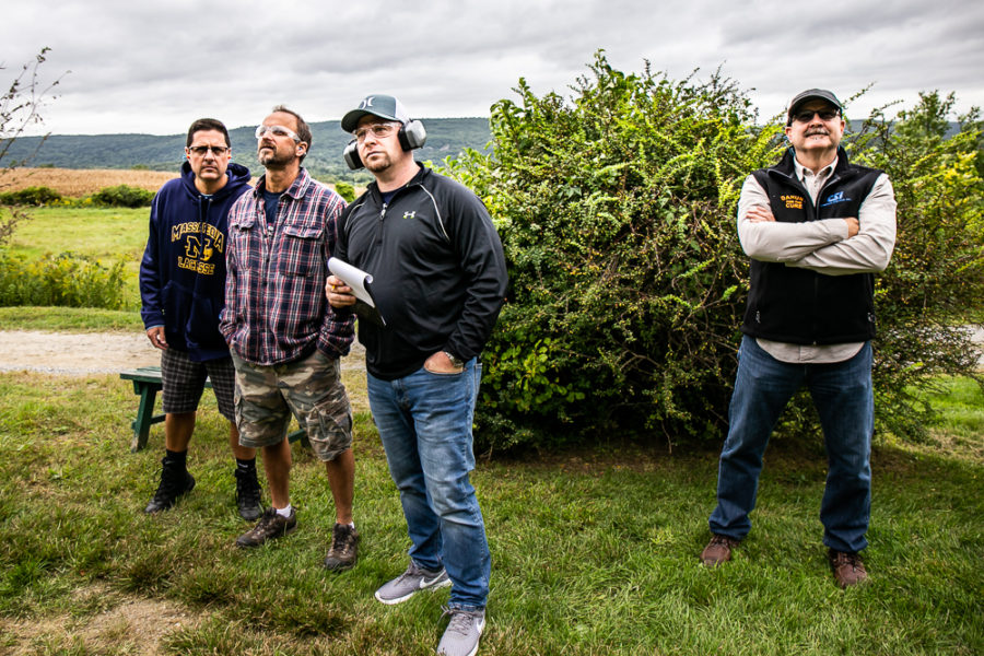 Four men standing outdoors near a bush.