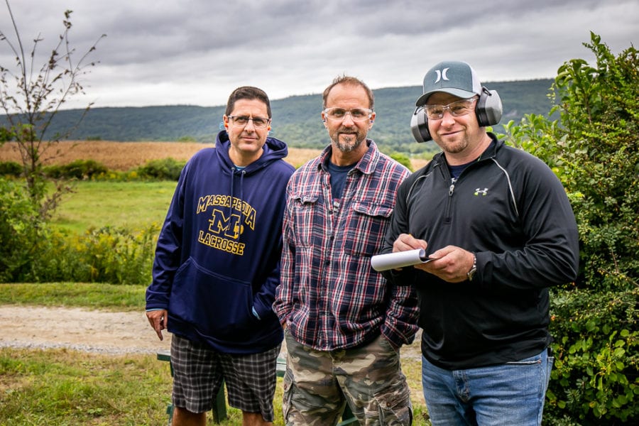 Three men standing in grassy rural field