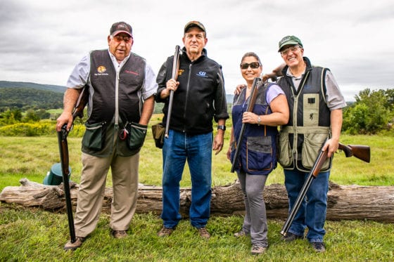 Four shotgun shooters posing in grassy field