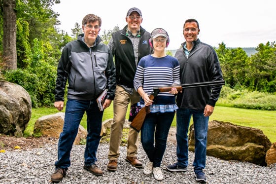Four people outdoors with woman holding shotgun