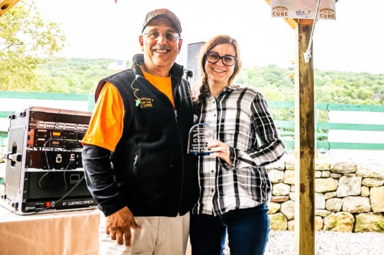 Two smiling people holding glass award outdoors