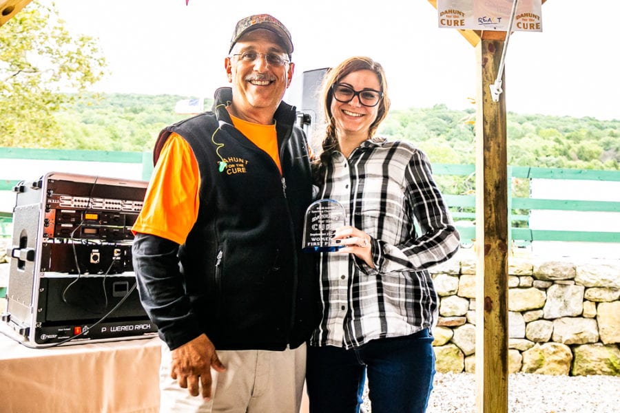 Two smiling people holding glass award outdoors