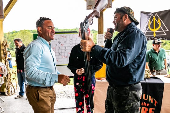 Men smiling during outdoor auction holding shotgun