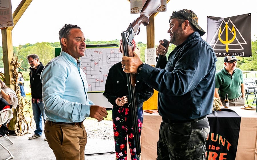 Men smiling during outdoor auction holding shotgun
