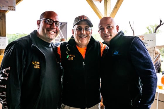 Three men smiling under pavilion with pumpkins