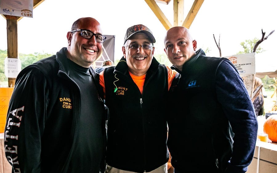 Three men smiling under pavilion with pumpkins