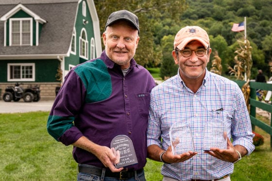 Two smiling men holding awards outside green barn