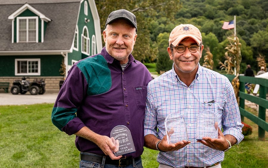 Two smiling men holding awards outside green barn