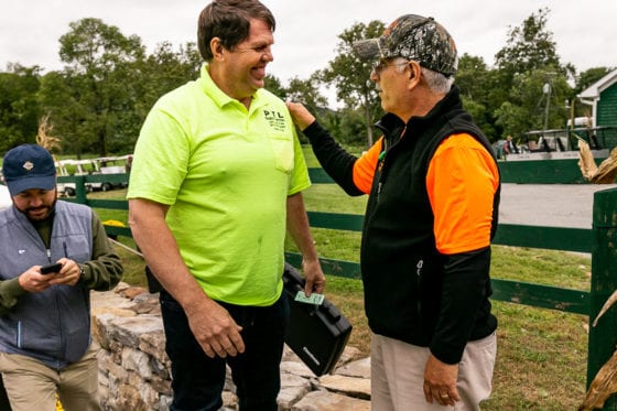 Three men greeting outdoors by farm fence