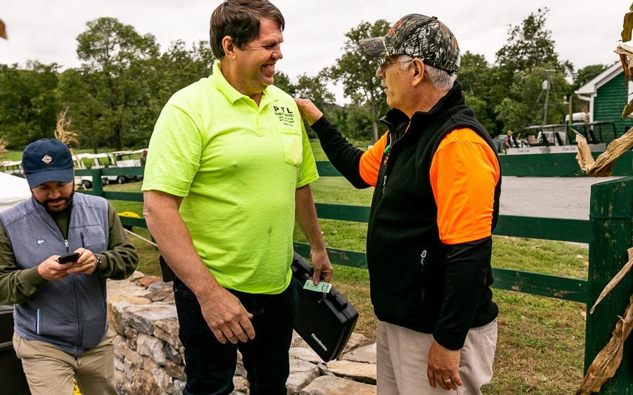 Three men greeting outdoors by farm fence