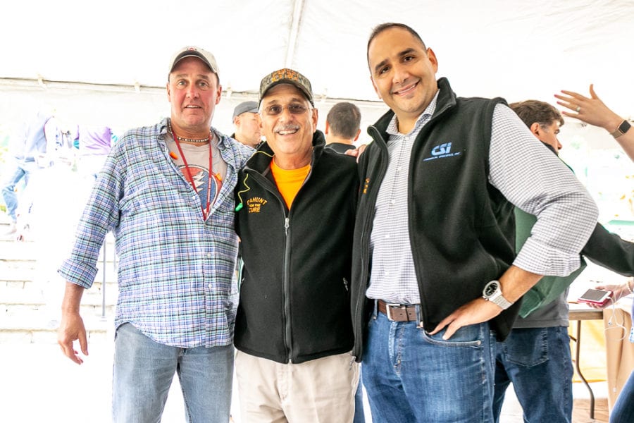 Three smiling men posing under outdoor event tent