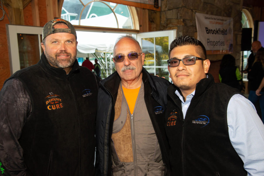 Three men in matching black vests indoors