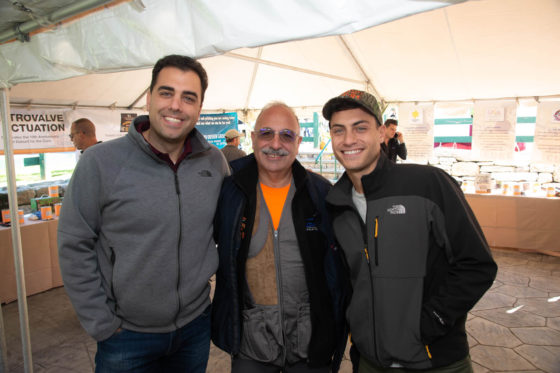 Three smiling men posing under market tent