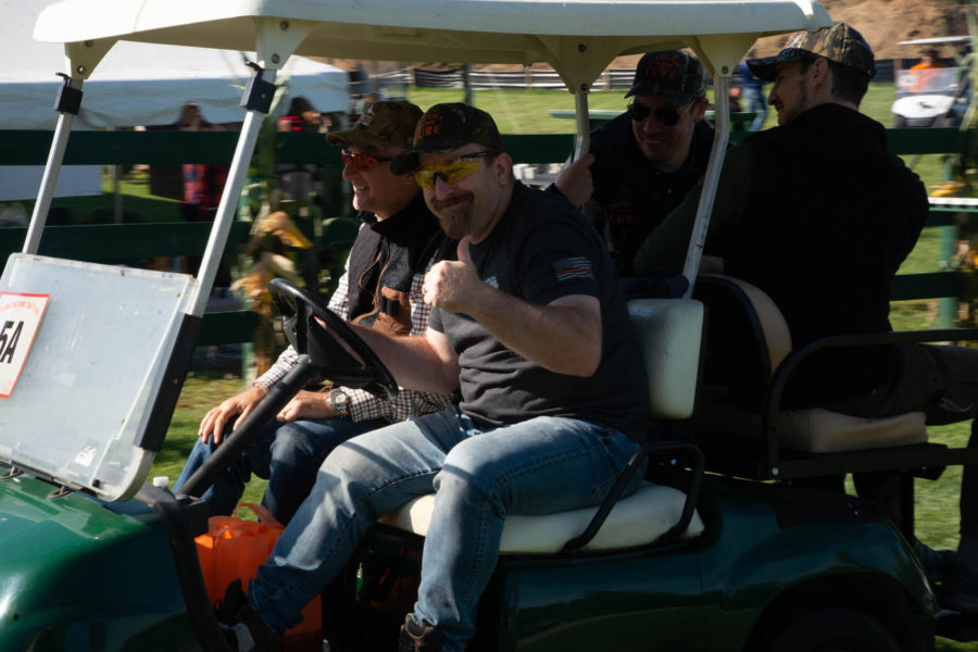 People riding golf cart, driver giving thumbs-up