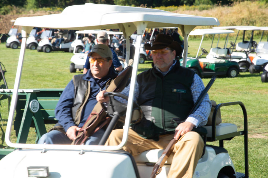 Two men in golf cart holding shotguns