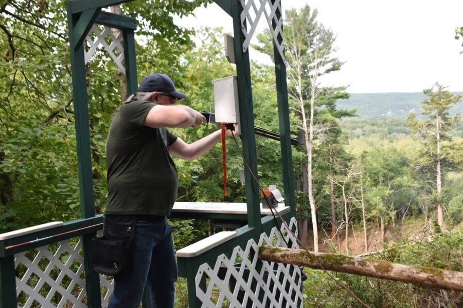 Man installing white birdhouse on wooden gazebo