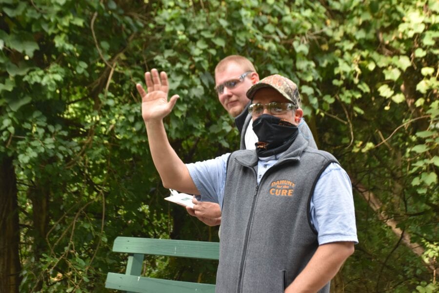 Masked man waving beside bench in park