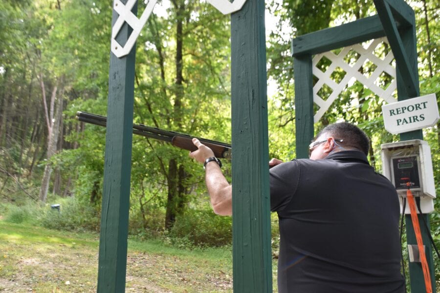 Man shooting shotgun at outdoor skeet range