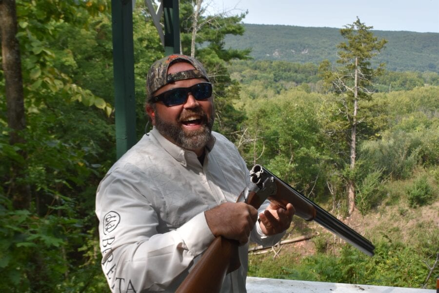 Smiling man holding shotgun at outdoor range