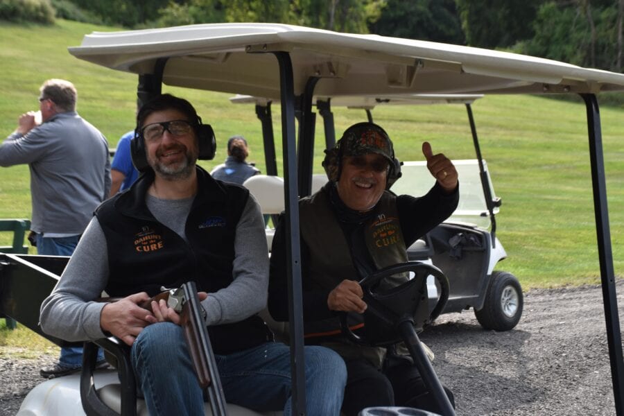 Two men smiling in golf cart with shotguns