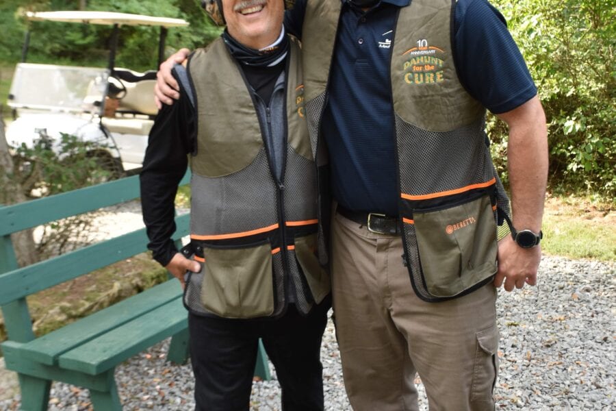 Two men in outdoor shooting vests smiling