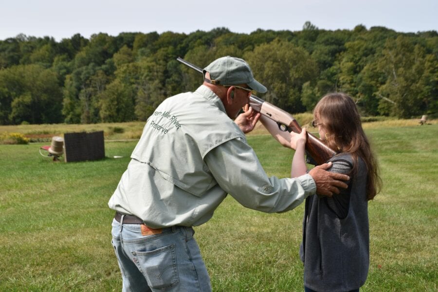 Instructor teaching girl to shoot shotgun outdoors