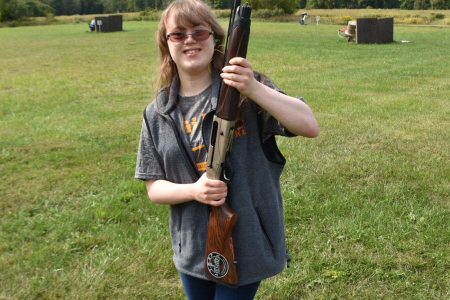 Smiling person holding shotgun at outdoor range