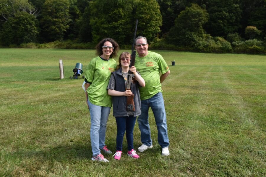 Three people in grassy field holding shotgun