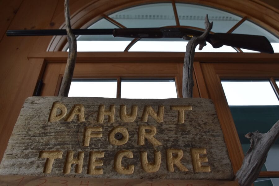Sign "Da Hunt for the Cure" under rifle