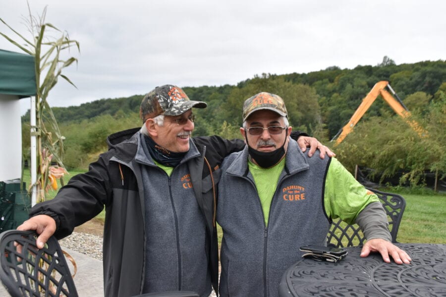 Two men wearing camo caps, matching vests smiling