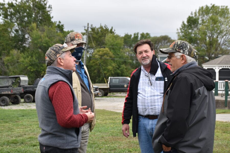 Four men talking outdoors near vehicles