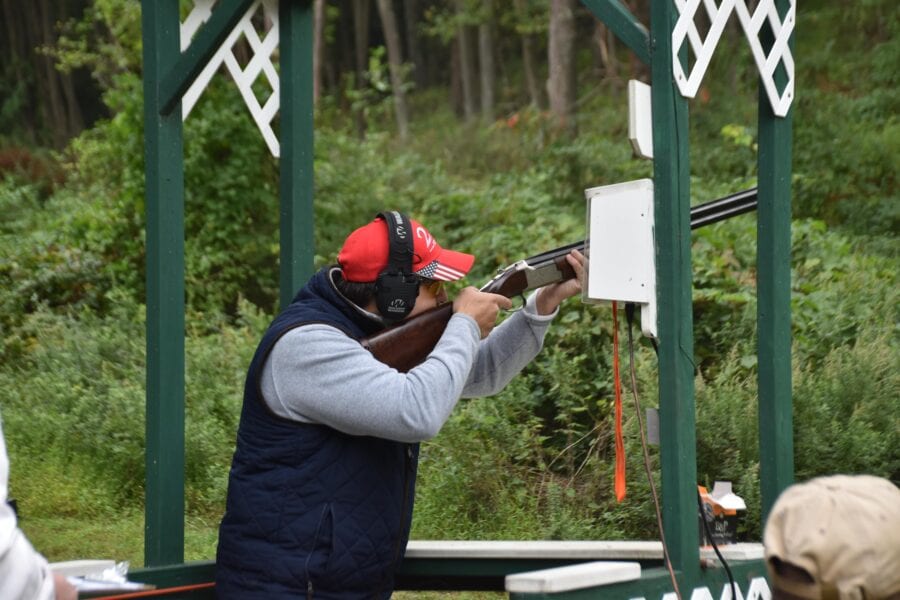 Shooter aiming shotgun at outdoor skeet range
