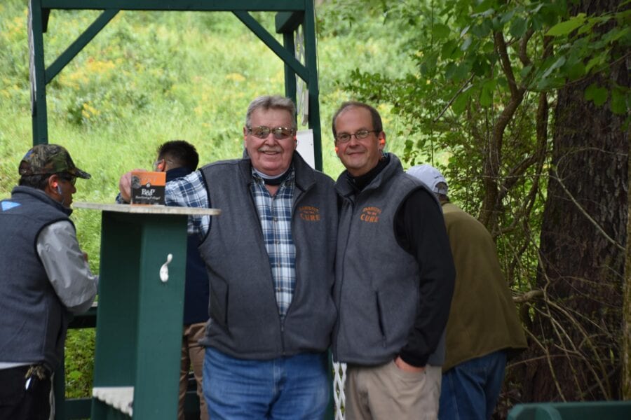 Two smiling men in matching vests outdoors