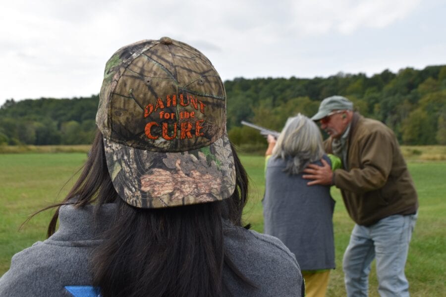 Camo hat in foreground, couple hugging in field