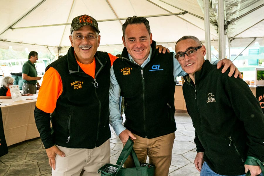 Three smiling men posing under event tent