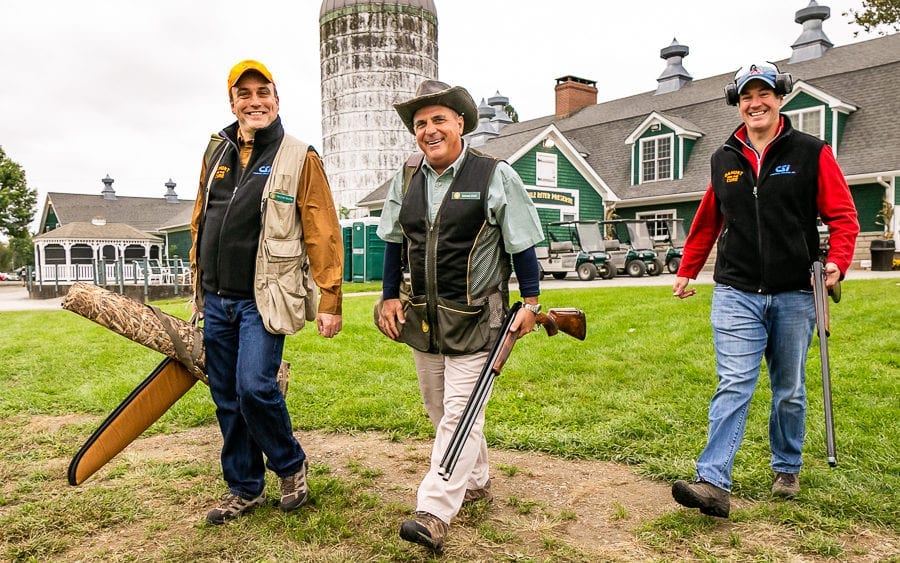Three hunters walking with shotguns near barn