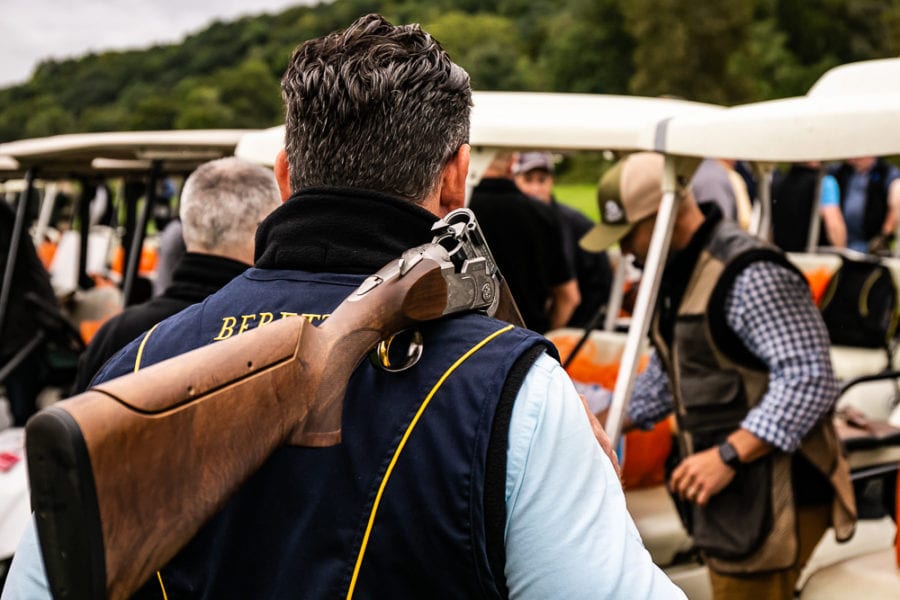 Man carrying shotgun over shoulder near golf carts