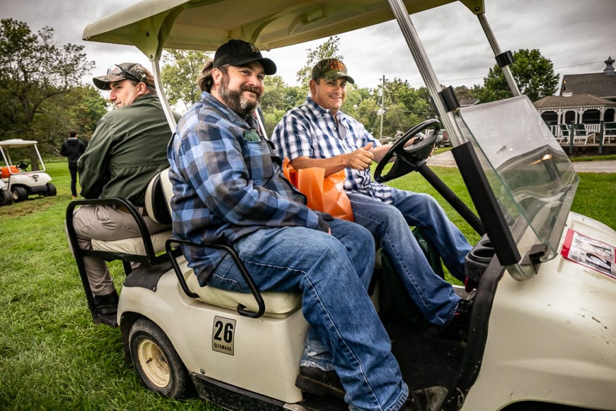Three smiling men riding a golf cart