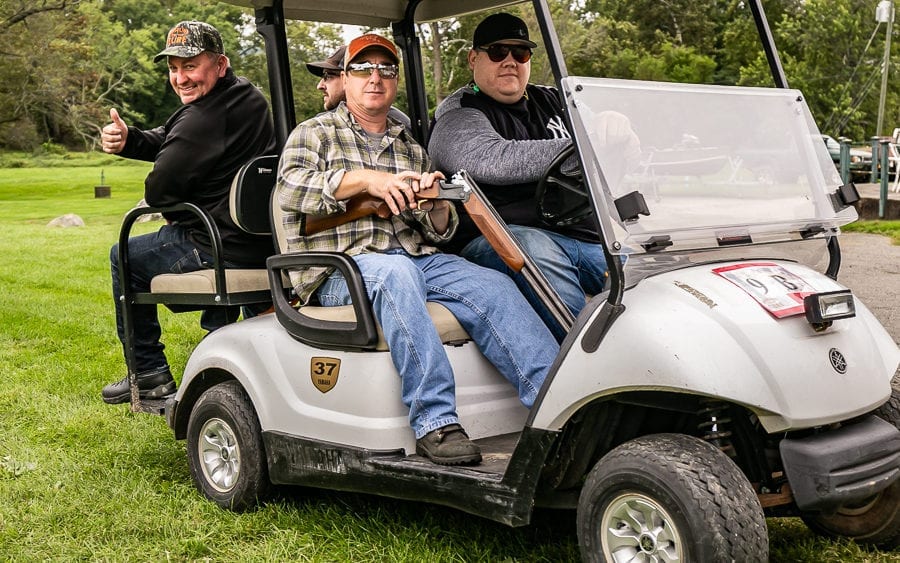 Three men in golf cart, one holding shotgun